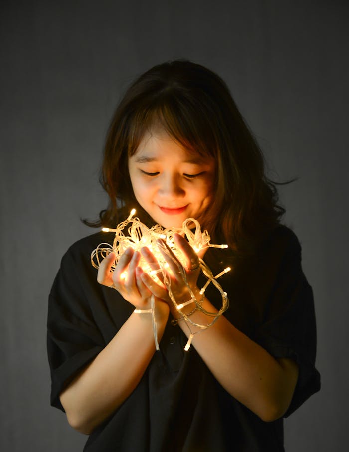 A woman joyfully holding glowing fairy lights indoors, creating a magical atmosphere.